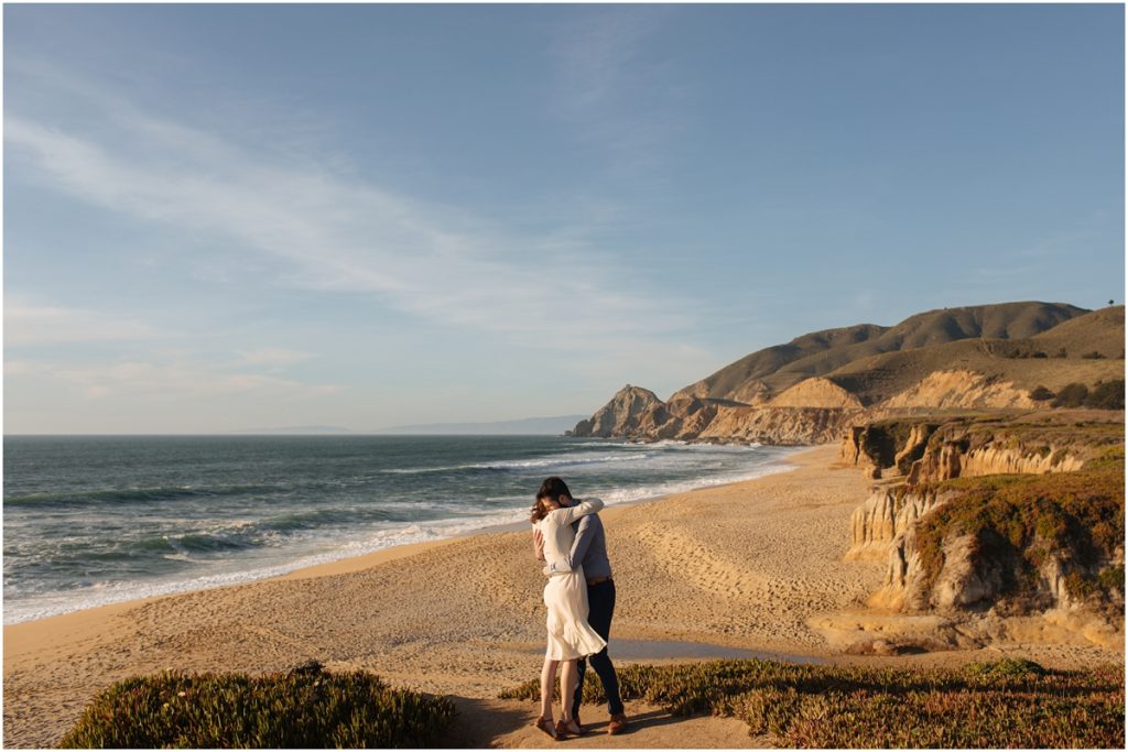 Couple embraces during their California engagement photos with an epic view behind them