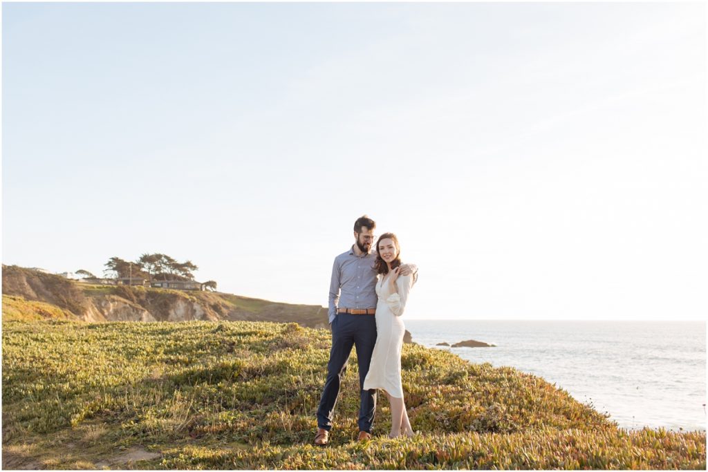 Man and woman hold each other other the cliff over the ocean during their California engagement photos