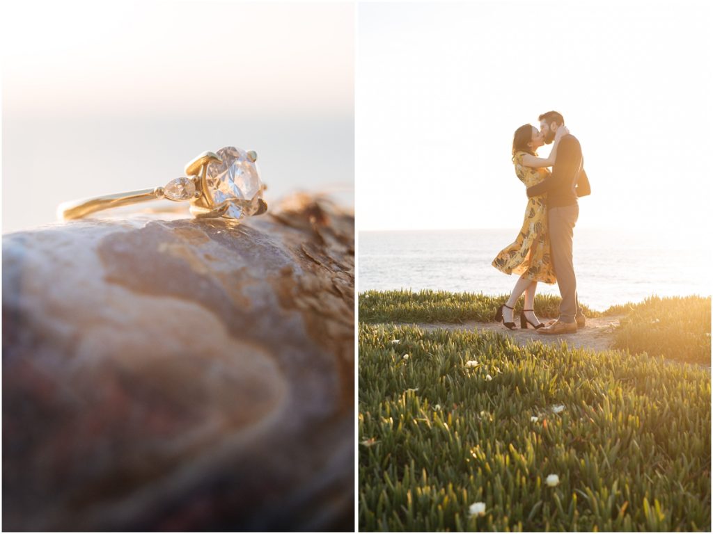 Striking diamond and gold ring with three prong diamonds sits on a shell during Couple embrace on the cliffs next to the ocean during Half Moon Bay engagement photos