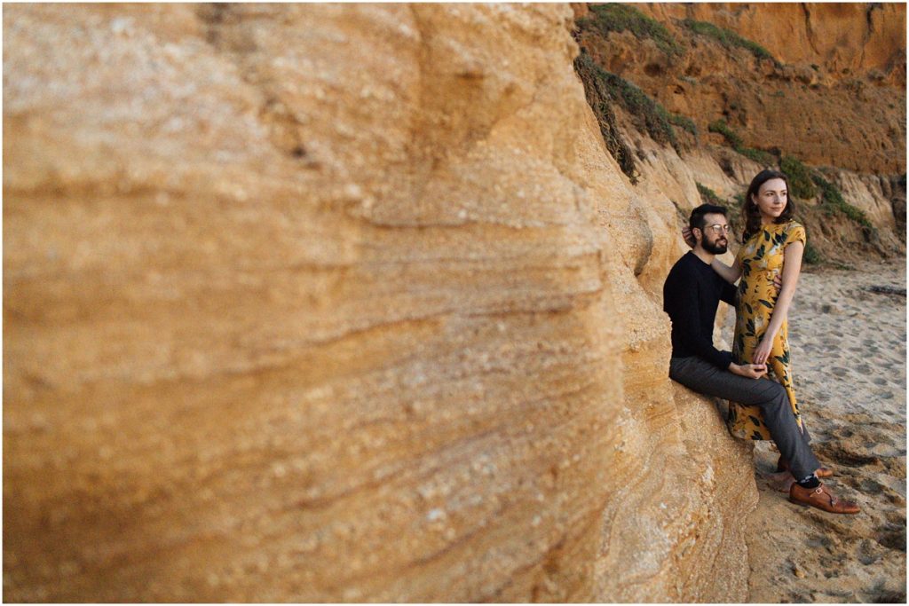 Couple sits together on the red cliffs during their Half Moon Bay engagement photos
