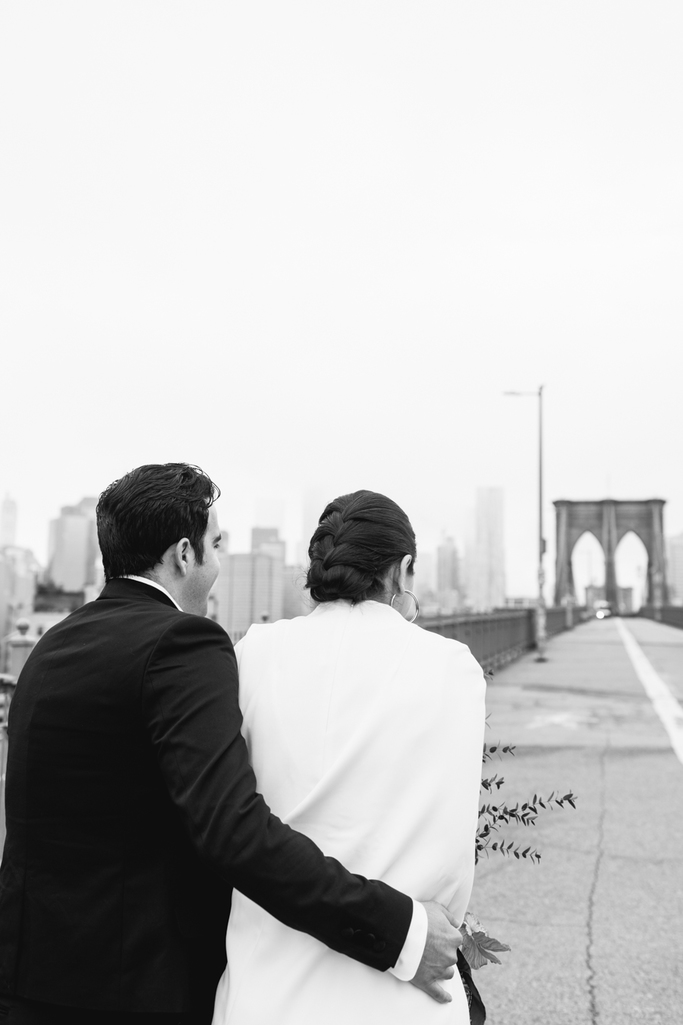 Groom has his arm around bride as they walk towards the Brooklyn Bridge for their Brooklyn elopement