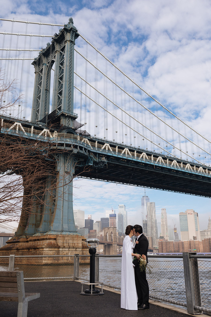 Bride and groom stand and embrace in front of the Manhattan Bridge during their morning Brooklyn elopement