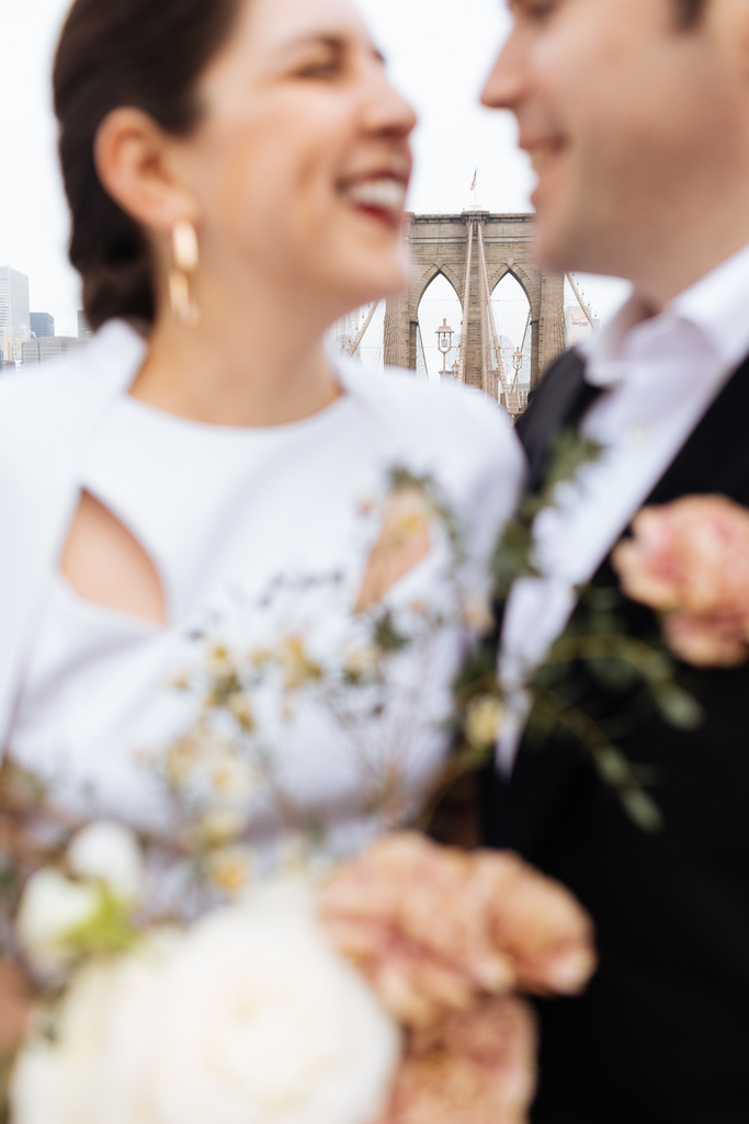 Bride and groom smile at each other with the Brooklyn Bridge behind them during their Brooklyn elopement