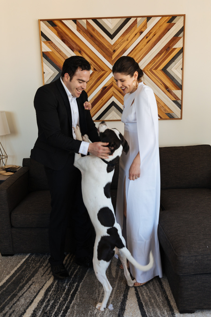 The bride and groom stand with their rescue pup in their apartment in Brooklyn after their Brooklyn elopement at sunrise
