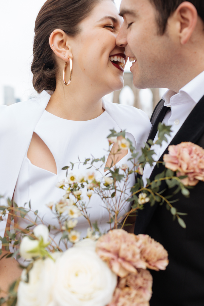 Bride and groom smile at each other and almost kiss with the Brooklyn Bridge behind them during their Brooklyn elopement