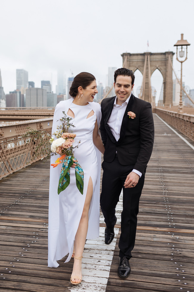 Bride and groom walk down the Brooklyn Bridge with their arms around each other after their Brooklyn elopement