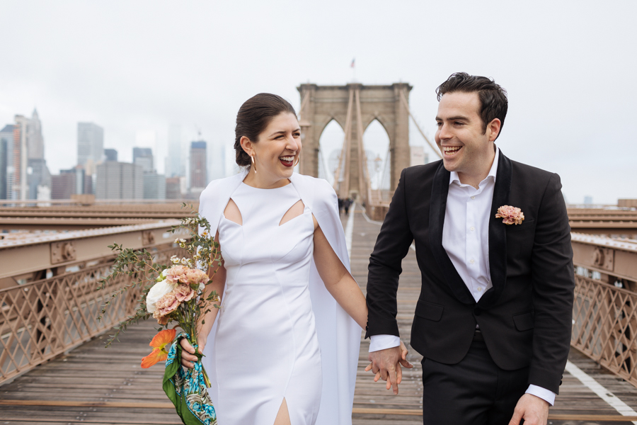 Bride and groom laugh together on the Brooklyn Bridge after their Brooklyn elopement