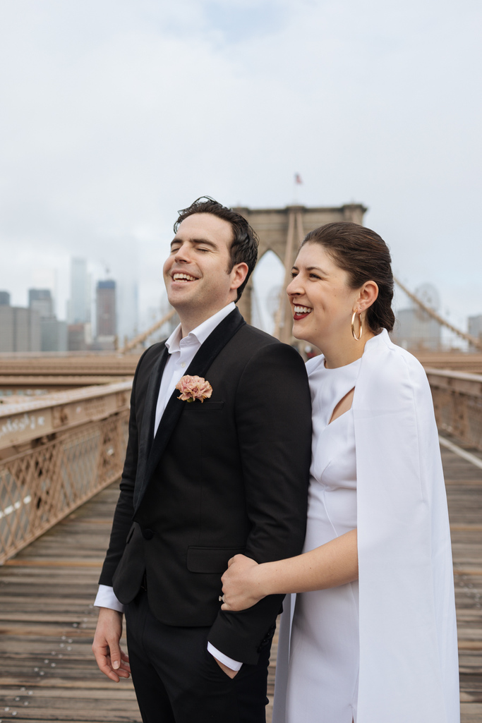 The groom laughs while the bride smiles after their Brooklyn elopement on the Brooklyn Bridge
