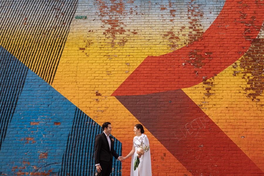Bride and groom stand in front of a bright and epic mural during their Brooklyn elopement in DUMBO