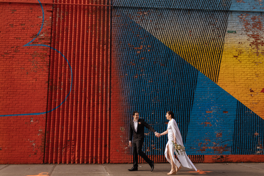 Bride and groom walk in front of a bright and epic mural during their Brooklyn elopement in DUMBO