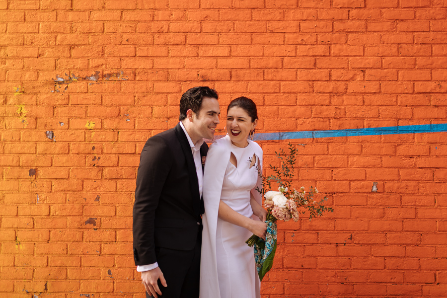Bride and groom laugh together in front of a bright and epic mural during their Brooklyn elopement in DUMBO