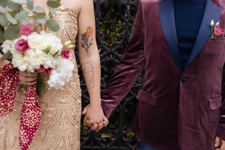 Bride and Groom hold hands and smile at each other in front of the Grace Church under a large blooming magnolia tree during their East Village elopement in NYC