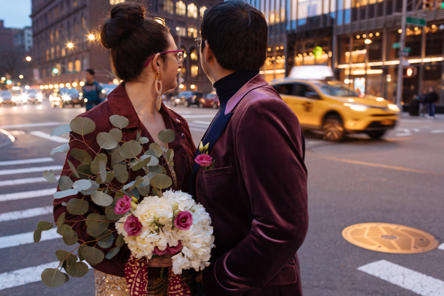 bride and groom stand under a street lamp at dusk in NYC during their West Village elopement and watch a taxi go by on the street