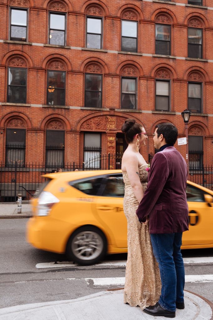 Bride and groom stand together during their East Village elopement while a yellow NYC taxi cab goes by