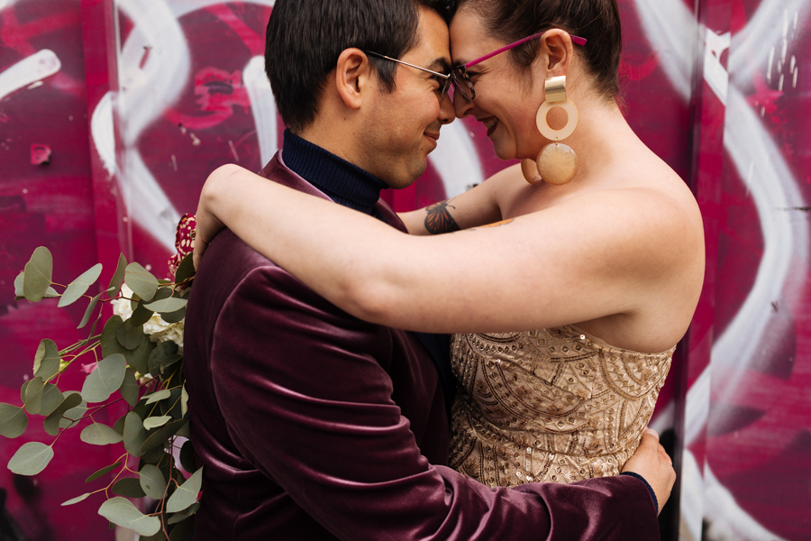 Bride and groom stand together embracing in front of pink graffiti during their East Village elopement
