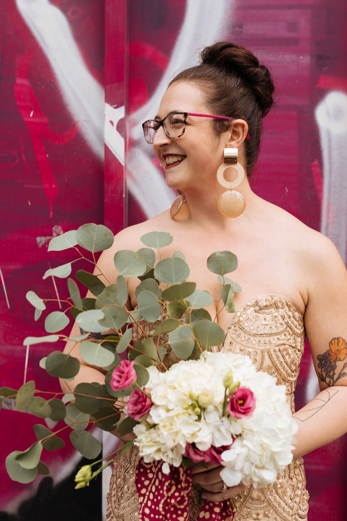 Bride smiles in front of bright pink graffiti art wall in NYC during her  East Village elopement