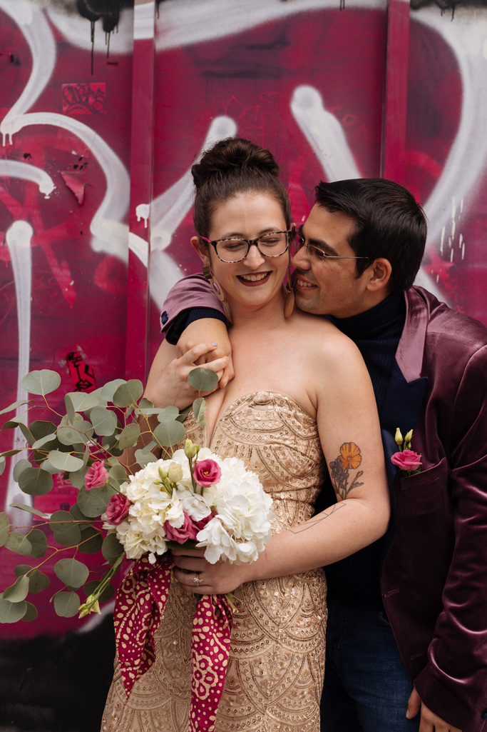 Bride and groom snuggle in front of bright pink graffiti wall in NYC during their East Village elopement