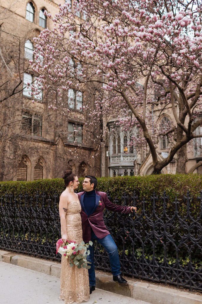 Bride and Groom stand in front of the Grace Church under a large blooming magnolia tree during their East Village elopement in NYC