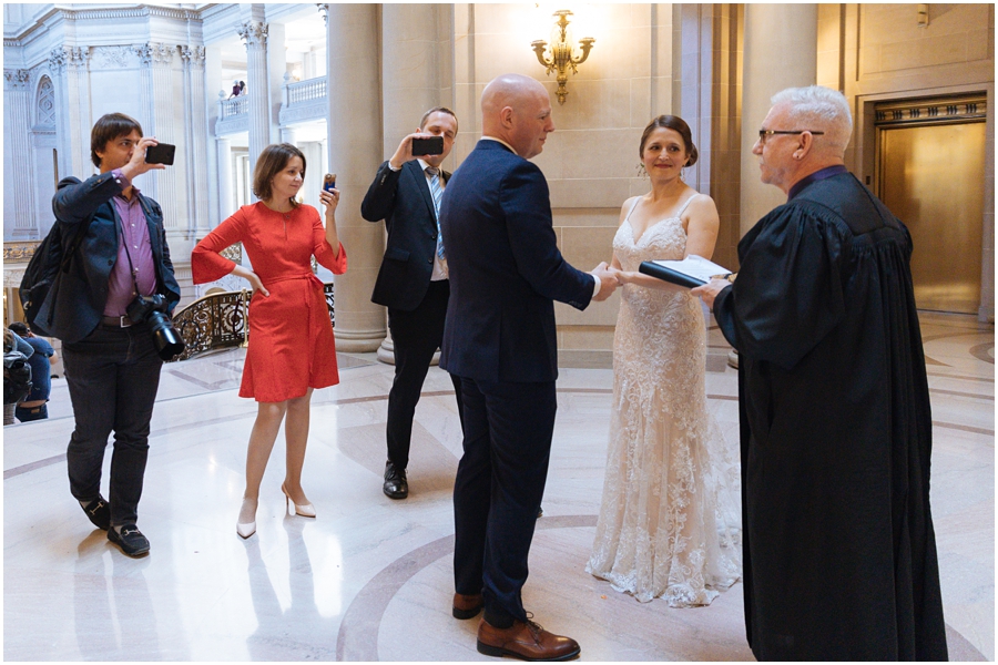 Couple holds hands while their family look on in the rotunda during their wedding ceremony at their San Francisco City Hall wedding in California