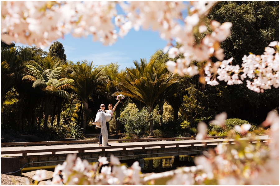 Groom holds bride on the bridge under the cherry blossoms during their San Francisco picnic wedding reception