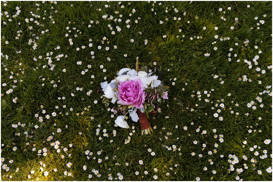 Bride's wedding bouquet with a big, pink peony sits on the grass and the daisies during her San Francisco picnic wedding