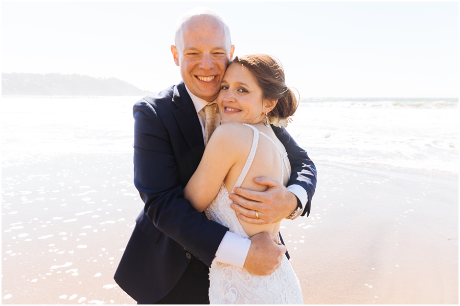 Bride and groom embrace in the waves at Baker Beach in front of the Golden Gate Bridge during their San Francisco picnic wedding on the beach