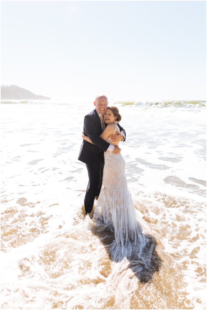 Bride and groom embrace in the waves at Baker Beach in front of the Golden Gate Bridge during their San Francisco picnic wedding on the beach