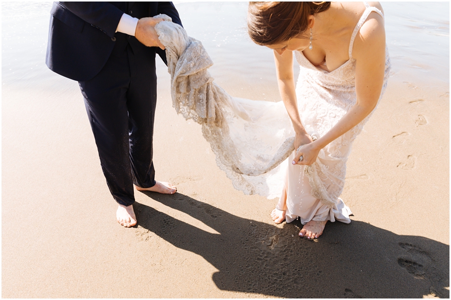 Bride squeezes ocean water out of her wedding dress at Baker Beach during her San Francisco picnic wedding