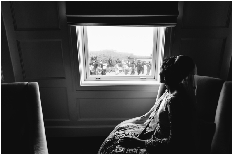 Bride looks out the window at the groom's processional during her Bride looks out the window at the groom's processional during her Half Moon Bay wedding at the Ritz Carlton at Half Moon Bay wedding venue the Ritz Carlton