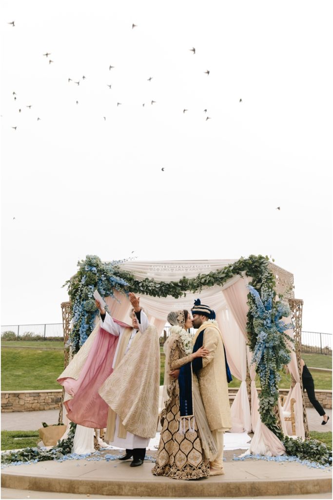 Couple has their first kiss while birds fly overhead during their wedding at their Half Moon Bay Ritz Carlton wedding