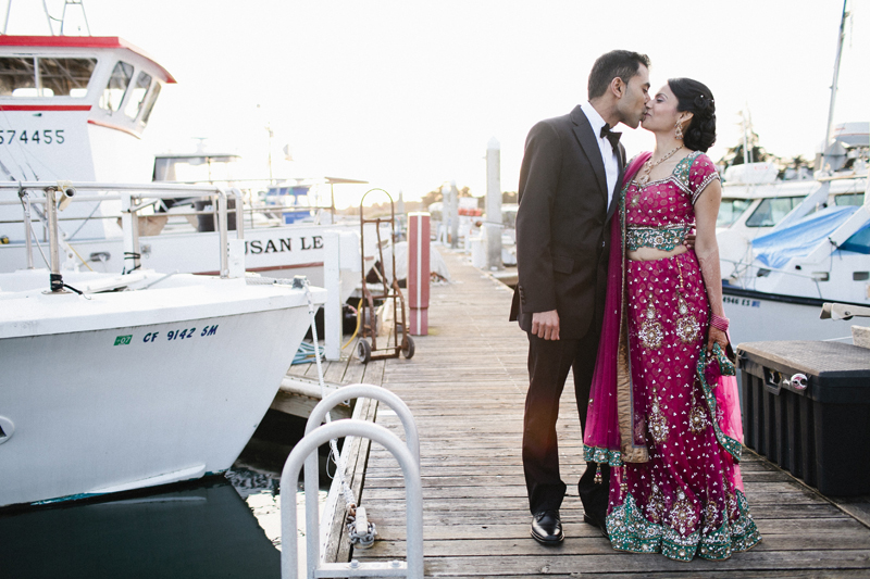Couple kisses during portraits at sunset in the harbor with the boats at Half Moon Bay wedding venue Oceano Hotel and Spa
